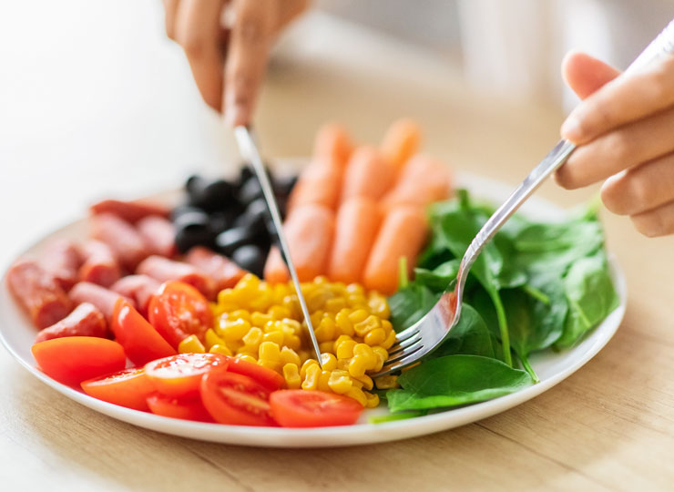 A person eating a platter of tomatoes, carrots, corn and leafy greens