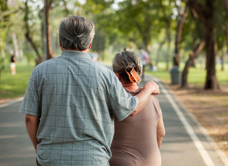 An older couple walking together along a tree-lined park path